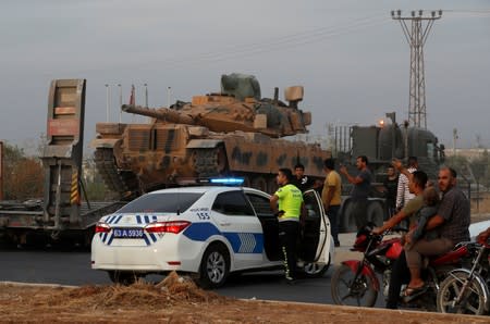 People wave as Turkish military vehicles pass by them in the Turkish border town of Akcakale in Sanliurfa province