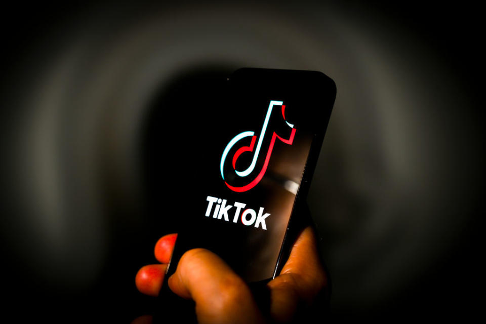 A hand holding a smartphone displaying the TikTok app logo prominently on the screen