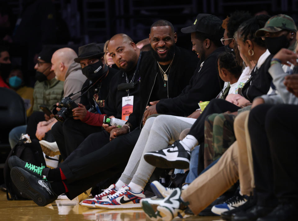 LeBron James sits courtside and laughs with other fans. 