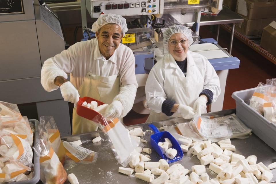 two workers in white coats, hair caps and white gloves show what they are bagging