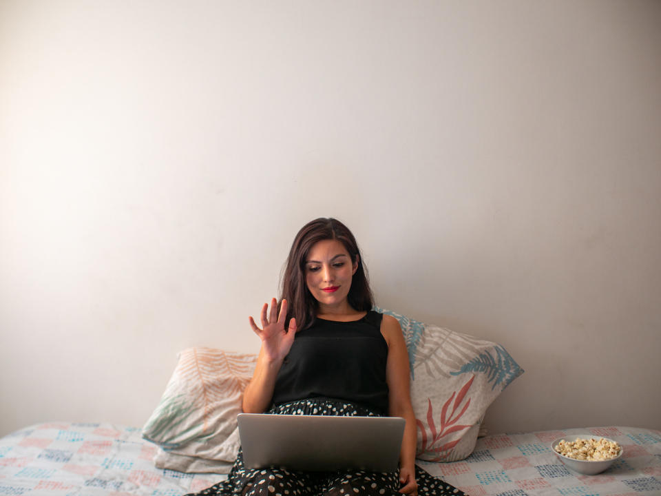 person on laptop in bed waving at screen