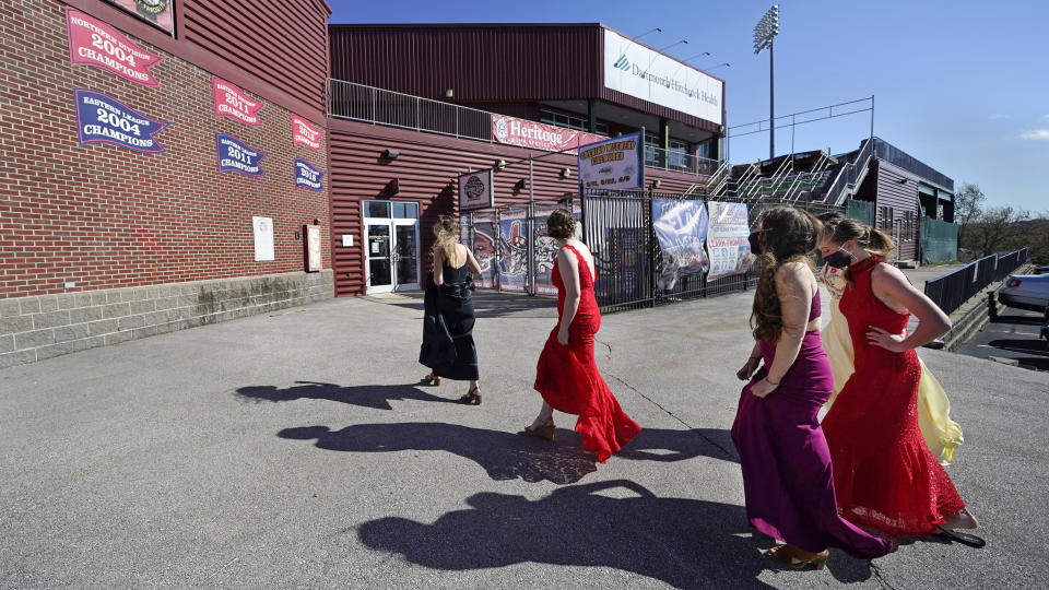 While wearing their prom gowns, students walk towards the entrance at the New Hampshire Fisher Cats minor league baseball stadium in Manchester, N.H., on Monday, April 26, 2021. After a year without proms, school districts across the country are debating whether they can safely hold an event that many seniors consider a capstone to their high school experience. The nearly 300 student senior class of Manchester's Central High School are waiting to get approval from the city's board of health so they can have their prom at the outdoor venue, due to COVID-19 concerns. (AP Photo/Charles Krupa)