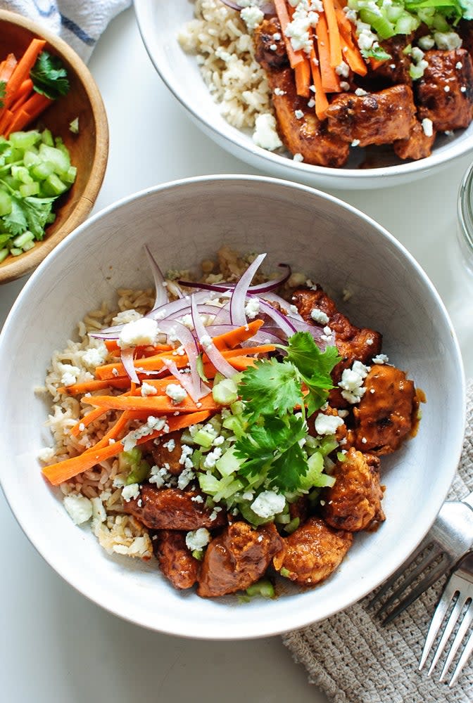 A bowl of rice topped with grilled chicken, carrots, red onions, and garnished with cilantro and crumbled cheese