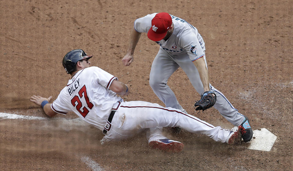 Atlanta Braves' Austin Riley (27) slides into home plate as Miami Marlins' Anthony Bass reaches for a tag during the 10th inning of a baseball game Sunday, July 4, 2021, in Atlanta. After a review of the play, the ruling on the field was overturned and Riley was called out. (AP Photo/Ben Margot)