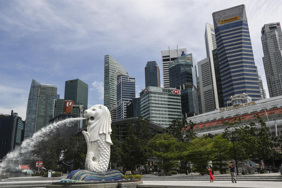 FILE - In this June 30, 2020, file photo, people are dwarfed against the financial skyline as they take photos of the Merlion statue along the Marina Bay area in Singapore. Singapore's economy entered recession in the April-June quarter, contracting by nearly 13% from the same period a year earlier. It contracted 41.2% in quarterly terms as the city-state, heavily reliant on trade and tourism, imposed “circuit breaker” precautions to curb the coronavirus pandemic.(AP Photo/Yong Teck Lim, File)