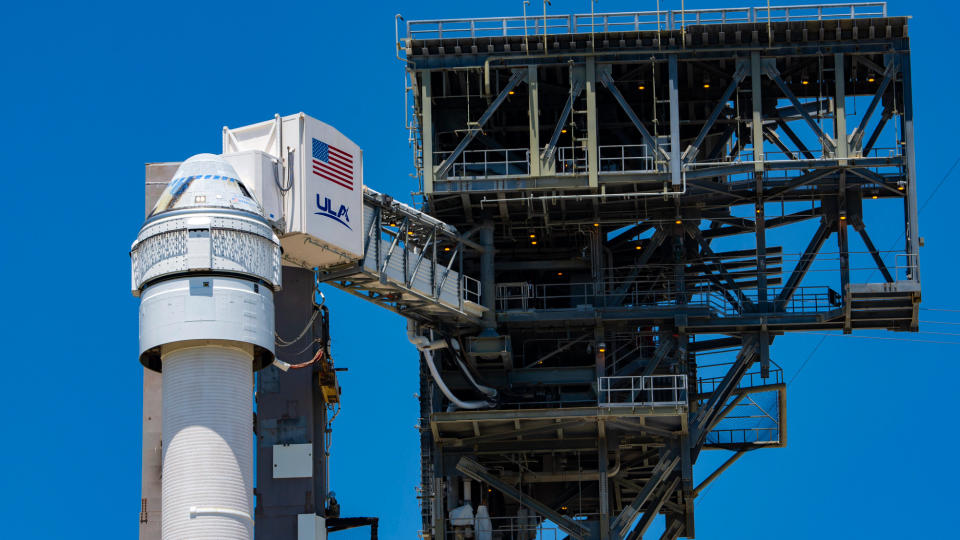 closeup of a white space capsule atop its rocket with a launch tower in the background