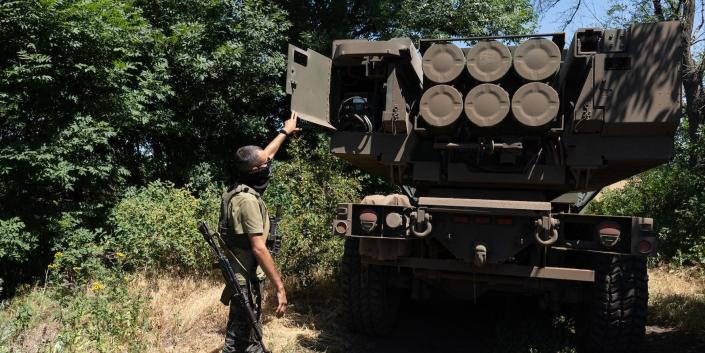 یک سرباز اوکراینی راکت ها را بر روی یک وسیله نقلیه HIMARS بین چند درخت نشان می دهد