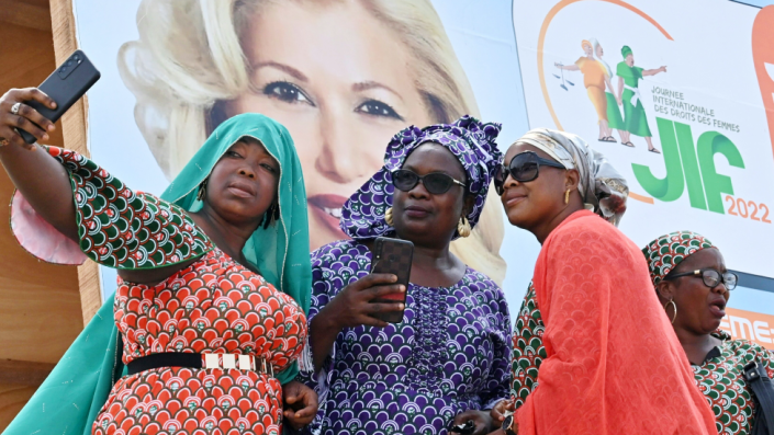 Women taking selfies in front of a International Women's Day poster showing the Ivorian first lady, Abidjan, Ivory Coast - Tuesday 8 March 2022
