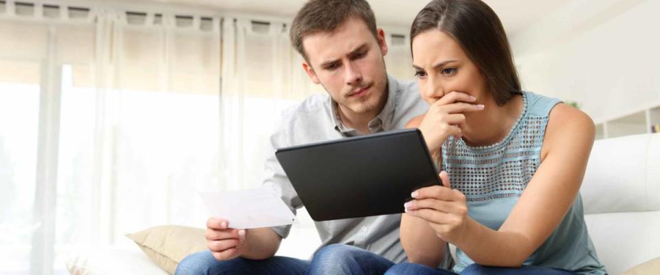 Worried couple checking bank account trouble online in a tablet sitting on a couch in the living room at home