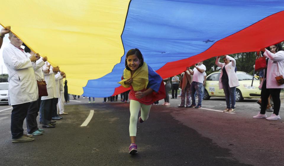 A girl runs under a Venezuelan flag held by Venezuelan doctors protesting the government of Venezuela's President Nicolas Maduro at the International Bridge Tienditas, which has been blocked by the Venezuelan military, near Cucuta, Colombia, Sunday, Feb. 10, 2019, across the border from Tachira, Venezuela. The doctors, who crossed into Colombia for the protest, are demanding their nation’s military allow humanitarian aid into the country, while Venezuelan President Nicolas Maduro contends the aid delivery is part of a larger U.S. intervention to remove him from power. (AP Photo/Fernando Vergara)