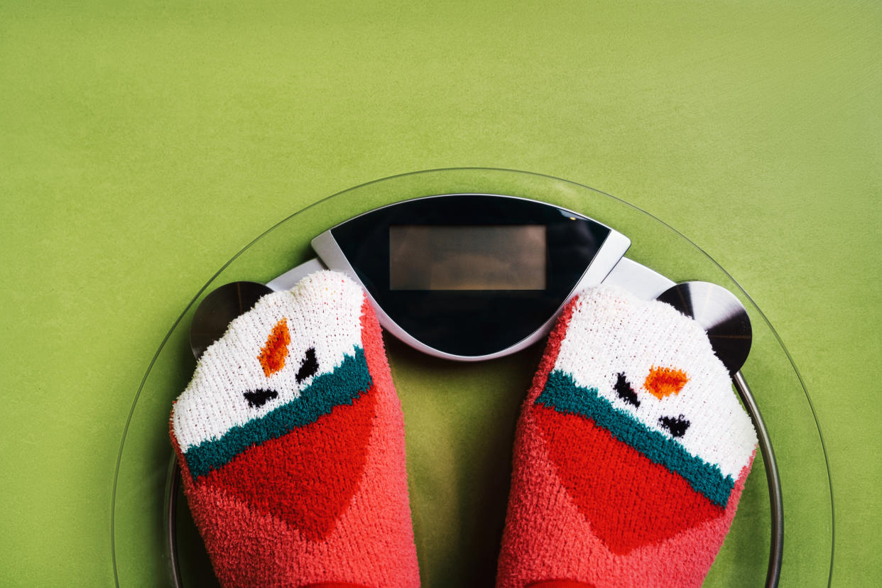 Girl standing on scale in Christmas fun red green socks with snowman background. 