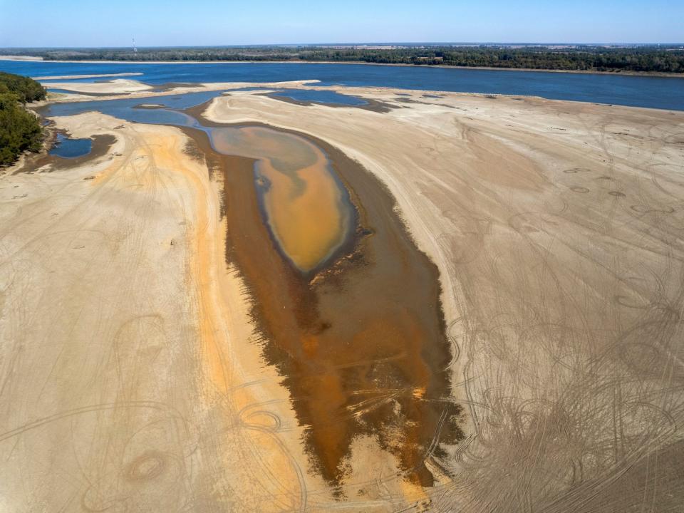 aerial image shows dry brown earth leading down to background river with a long patch of mud where water has recently dried