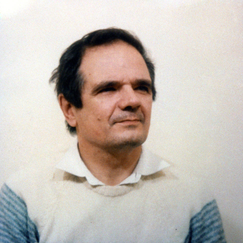 Middle-aged man with short dark hair, wearing a collared shirt under a light sweater, looking slightly up and to his right against a plain background