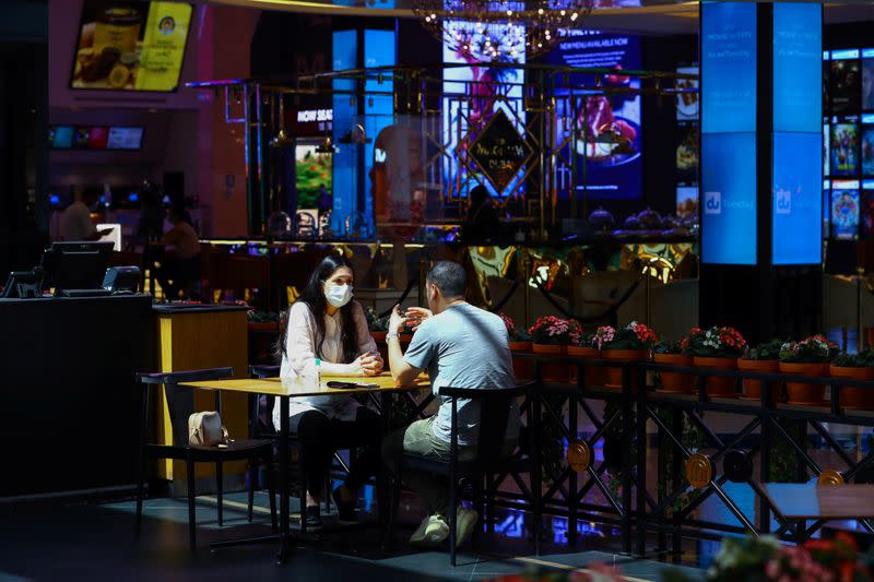 A woman wears a protective face mask as she sits with her friend in a coffee shop during the reopening of malls, following the outbreak of the coronavirus disease (COVID-19), at Mall of the Emirates in Dubai
