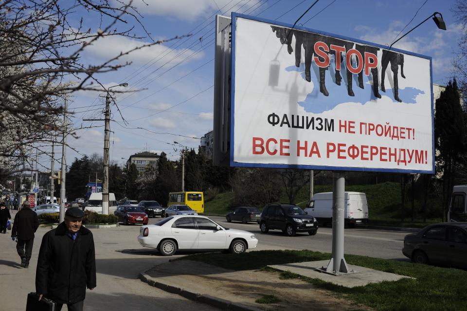 People walk by a poster reading "Fascism won't succeed. Everybody to the referendum!" in Sevastopol, Thursday, March 13, 2014. Crimea plans to hold a referendum on upcoming Sunday that will ask residents if they want the territory to become part of Russia. Ukraine's government and Western nations have denounced the referendum as illegitimate and warned Russia against trying to annex Crimea. (AP Photo/Andrew Lubimov)