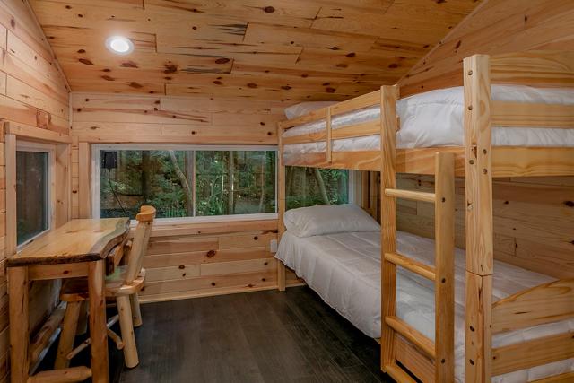 The upstairs bedroom has a bunk bed with views of the surrounding woods.