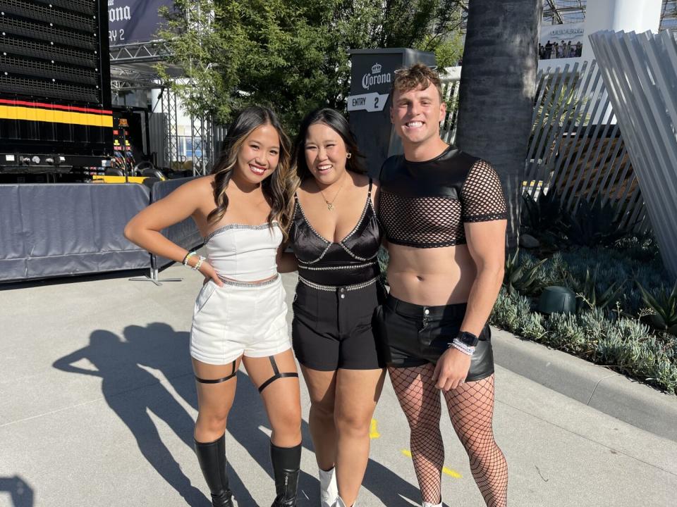 Three people, one in a white shorts outfit, one in a black shorts outfit and another in mesh black top and fishnet hose.