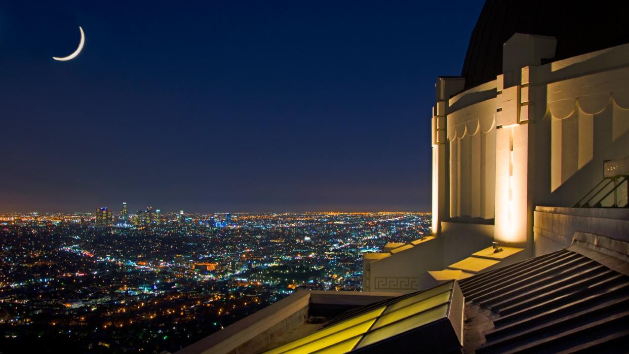  A white building with a large dome in the center lit up at night with city lights behind it. 