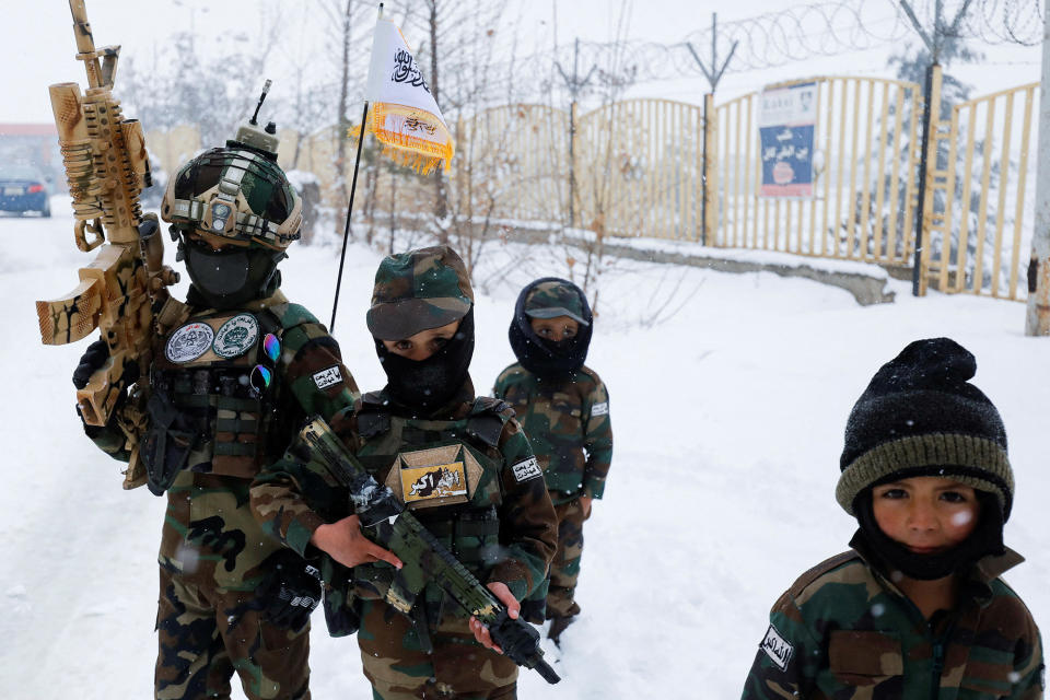 small children dressed head to toe in camo holding machine guns stand outside in the snow