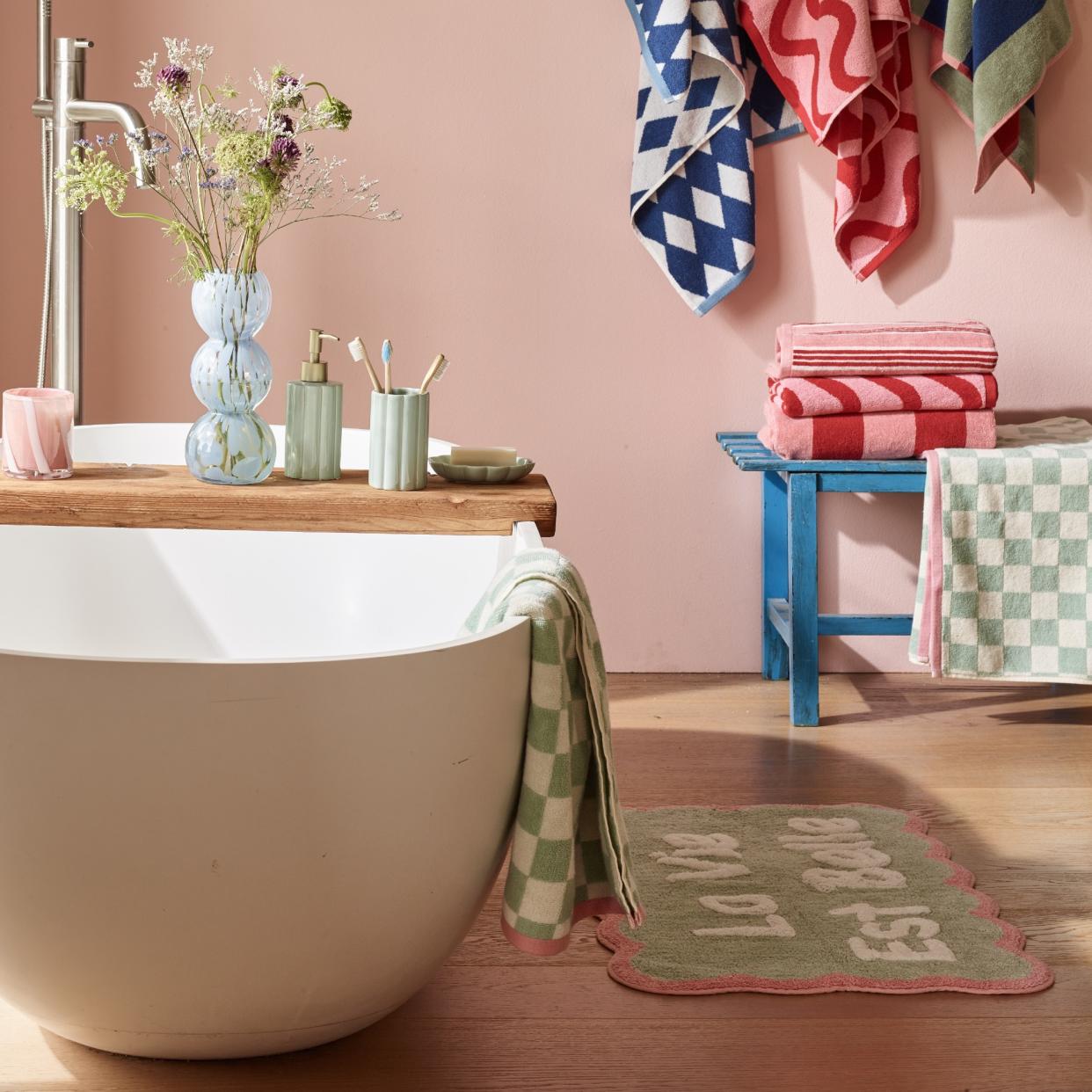  Pink bathroom with a bathtub and colourful, patterned towels and bath mat. 