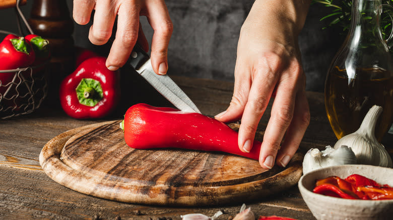 Hands cutting peppers on cutting board 