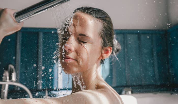 A woman with her eyes closed enjoys a refreshing shower, with drops of water falling on her face