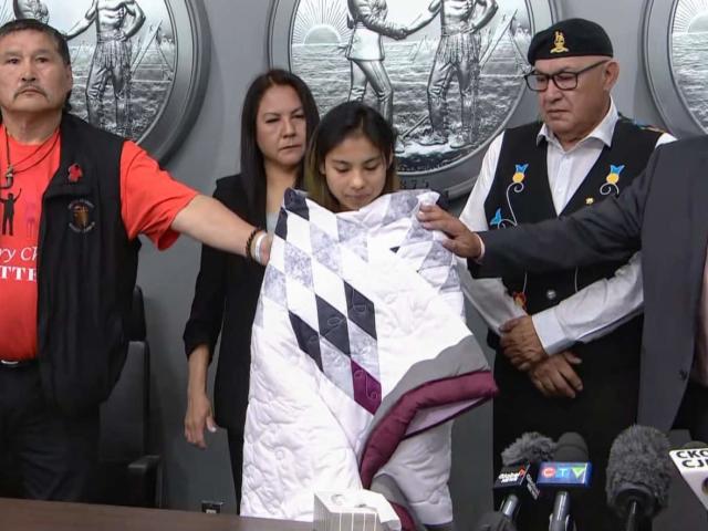 Kyla Frenchman is wrapped in a ceremonial blanket following a news conference regarding the death of her child, Tanner Brass. With Frenchman, from left to right, are Prince Albert Grand Council Chief Brian Hardlotte, Frenchman&#39;s lawyer Eleanore Sunchild, Federation of Sovereign Indigenous Nations (FSIN) vice-chief Edward Lerat and FSIN Chief Bobby Cameron. (CBC - image credit)
