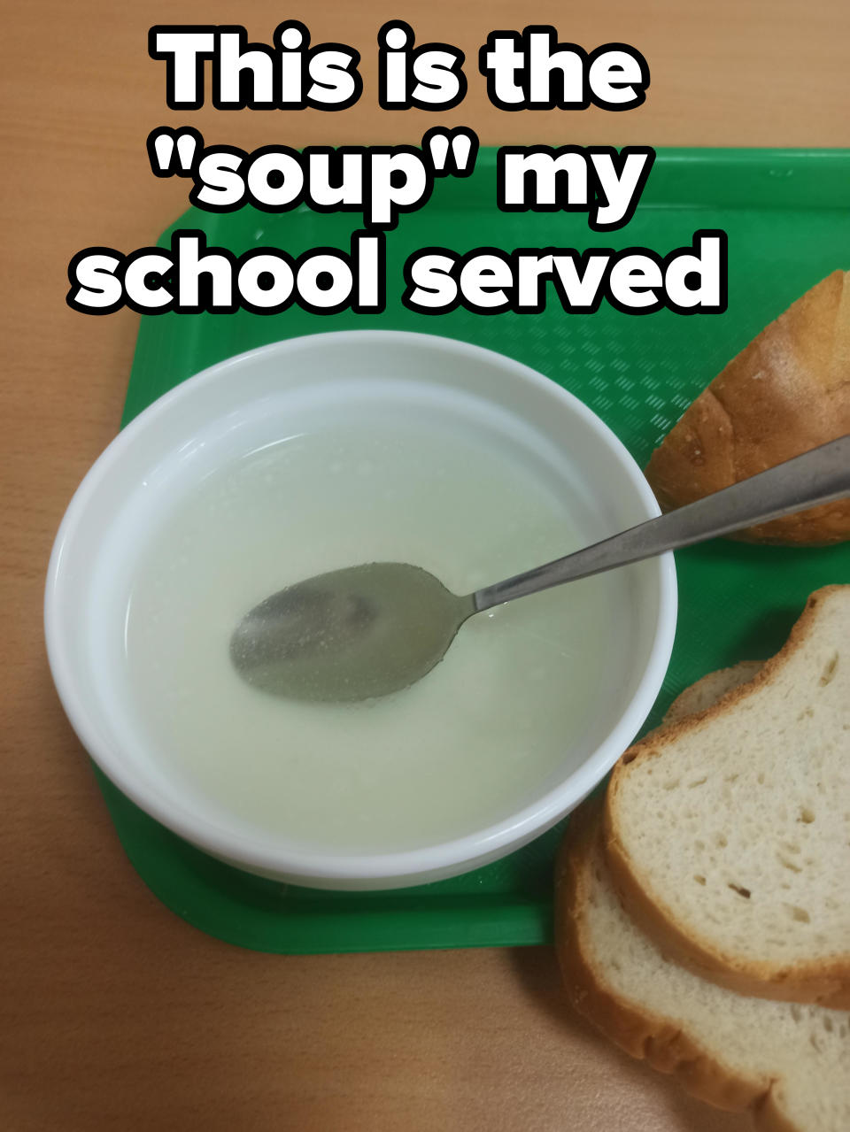 Bowl of soup with a spoon, slices of bread on a green tray, on a wooden table