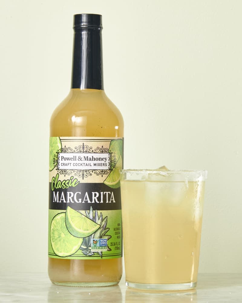 photo of Powell & Mahoney Classic Margarita mix bottle with a mixed drink next to it on a marble surface with a light green background