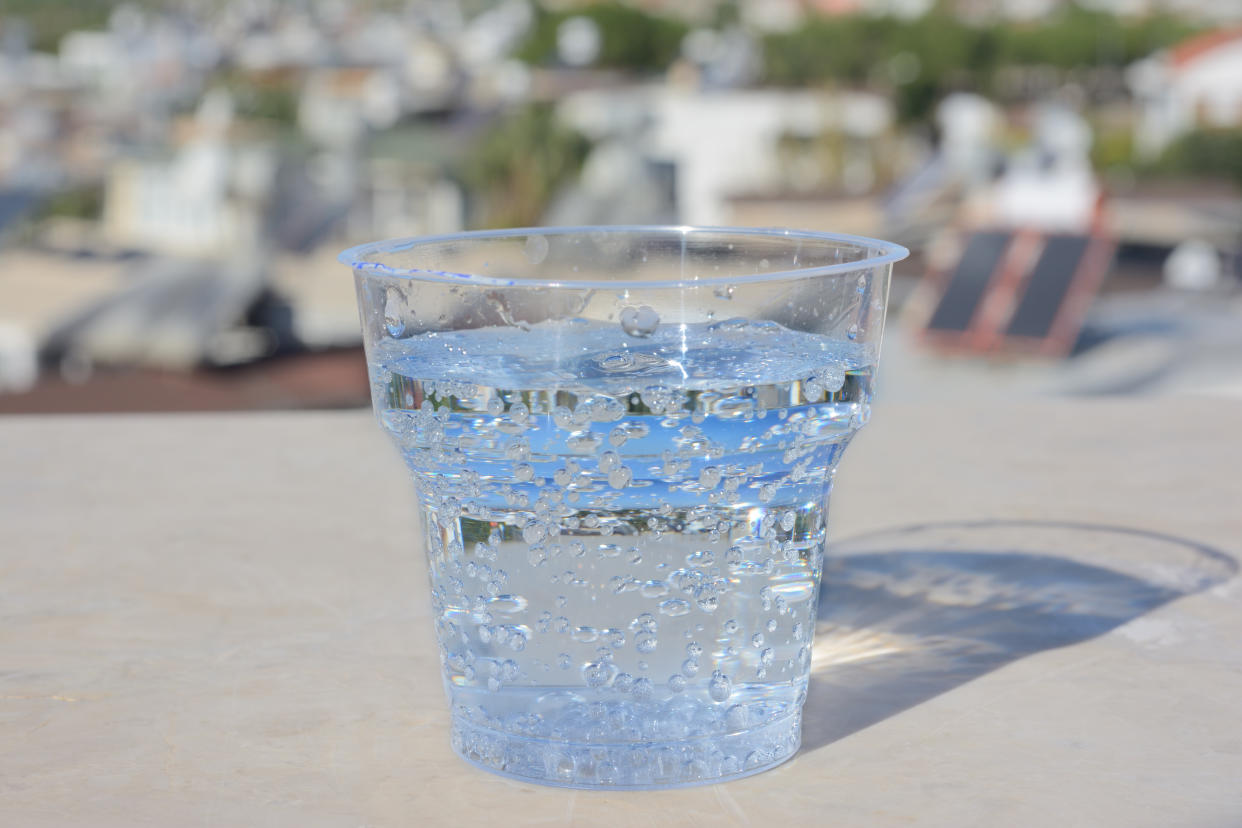 Transparent plastic, disposable glass with mineral water and gas bubbles. On the table against the background of a blurry view of the city