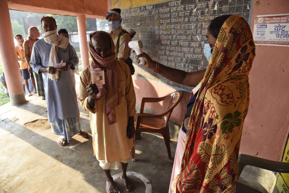 A woman wearing a face mask as a protective measure against the coronavirus screens the body temperature of voters at a polling station, during the first phase of state elections at Paliganj, in the eastern Indian state of Bihar, Wednesday, Oct. 28, 2020. With an overall declining coronavirus positive trend, Indian authorities decided to hold the first state legislature election since the outbreak of COVID-19. People began voting Wednesday in the country’s third largest state Bihar with of a population of about 122 million people. (AP Photo/Aftab Alam Siddiqui)