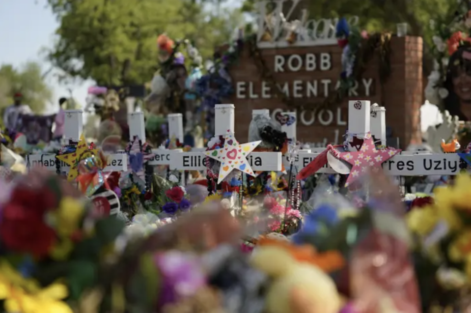 Crosses with victims' names are decorated in front of the Robb Elementary School sign