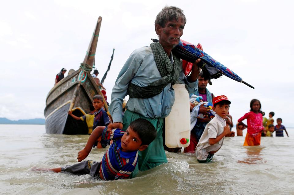 A Rohingya refugee man pulls a child as they walk to the shore after crossing the Bangladesh-Myanmar border by boat through the Bay of Bengal in Shah Porir Dwip, Bangladesh, September 10, 2017