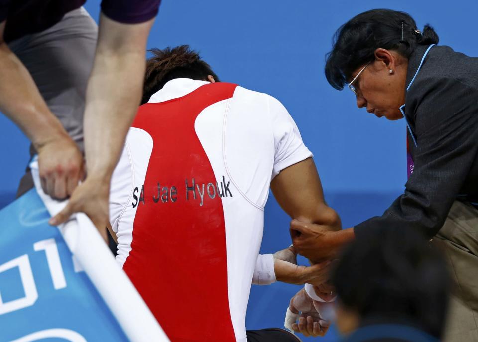 South Korea's Jaehyouk Sa is assisted after getting injured on the men's 77Kg Group A weightlifting competition at the ExCel venue at the London 2012 Olympic Games August 1, 2012. REUTERS/Grigory Dukor (BRITAIN - Tags: SPORT OLYMPICS SPORT WEIGHTLIFTING)