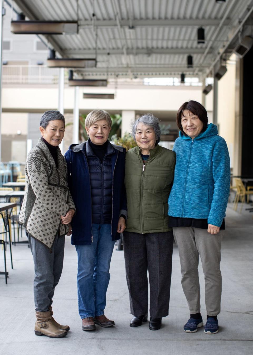 Certical image of four women standing side by side, posing for the photo, slightly smiling.