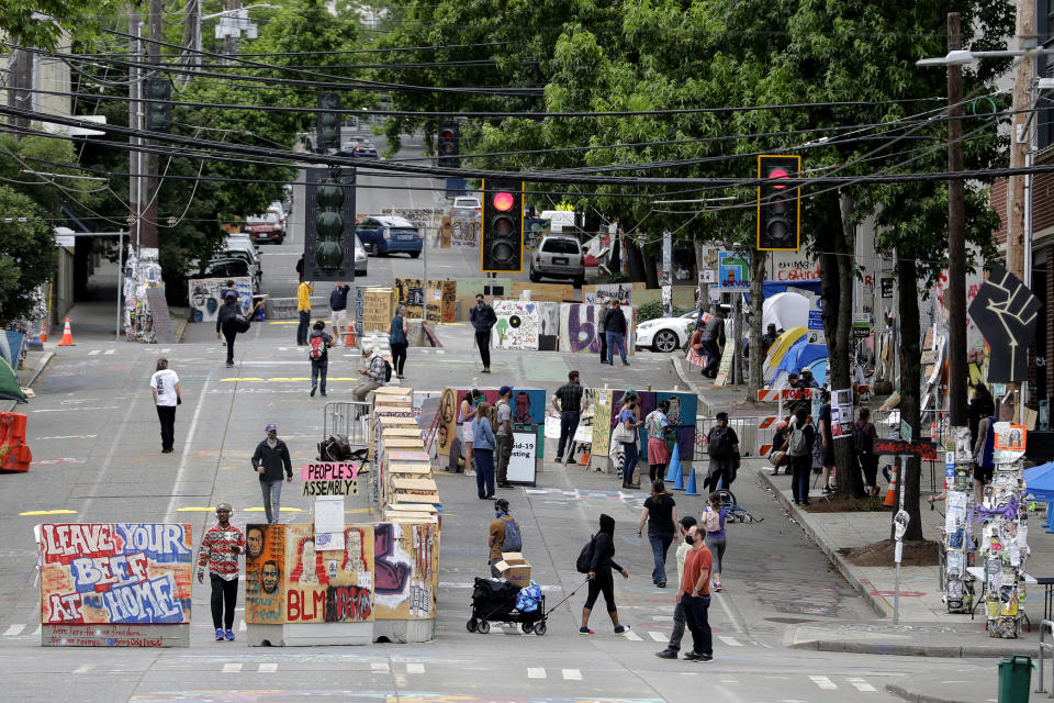 Visitors walk by the barricades, Wednesday, June 24, 2020, near the Seattle Police East Precinct building inside the CHOP (Capitol Hill Occupied Protest) zone in Seattle. The area has been occupied since a police station was largely abandoned after clashes with protesters, but Seattle Mayor Jenny Durkan said Monday that the city would move to wind down the protest zone following several nearby shootings and other incidents that have distracted from changes sought peaceful protesters opposing racial inequity and police brutality. (AP Photo/Ted S. Warren)