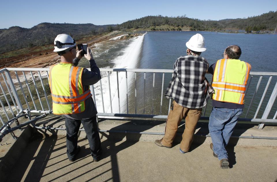 Jason Newton, left, of the Department of Water Resources, takes a picture of water going over the emergency spillway at Oroville Dam Saturday, Feb. 11, 2017, in Oroville, Calif. Water started flowing over the spillway,at the nation's tallest dam, for the first time Saturday morning after erosion damaged the Northern California dam's main spillway.(AP Photo/Rich Pedroncelli)