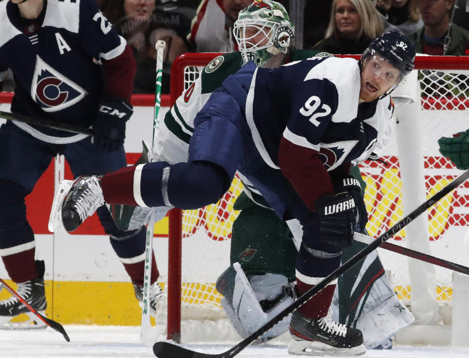 Colorado Avalanche left wing Gabriel Landeskog, front, struggles to stay on his skates as he looks for a pass while in front of Minnesota Wild goaltender Devan Dubnyk in the second period of an NHL hockey game Friday, Dec. 27, 2019, in Denver. (AP Photo/David Zalubowski)