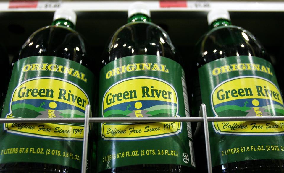 Bottles of Green River soda, featuring their signature green bottles and green-and-yellow labels, sit on a shelf at a supermarket