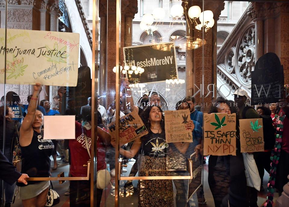 Protesters urging lawmakers to pass marijuana legislation hold signs against the state Senate lobby doors June 19 at the state Capitol in Albany.