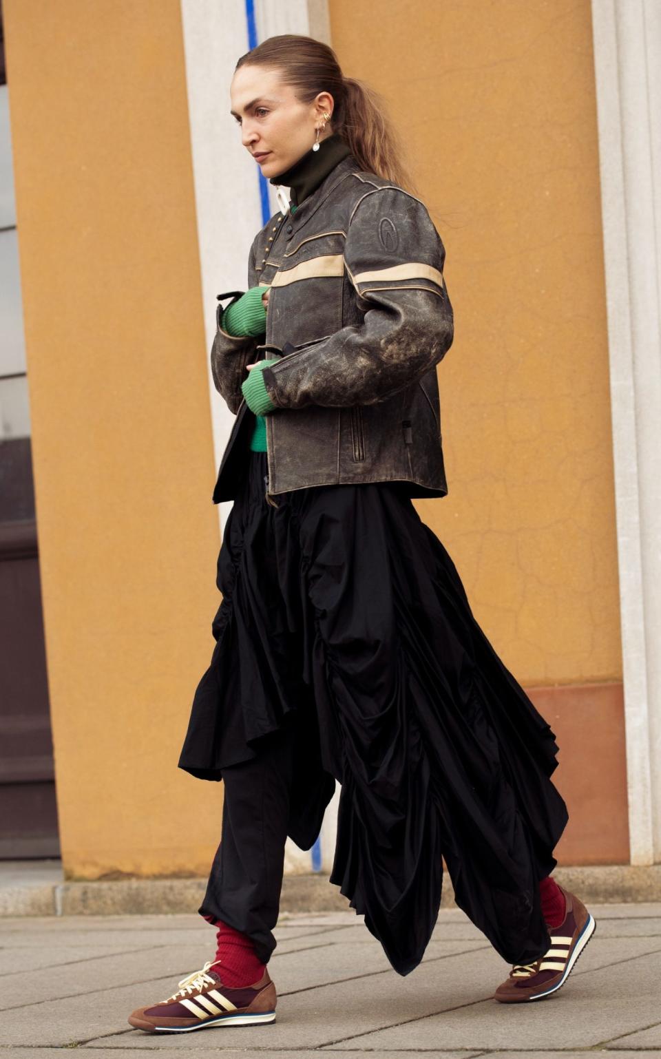 A guest at Copenhagen Fashion Week wearing a brown leather jacket, black skirt, brown sneakers and red socks