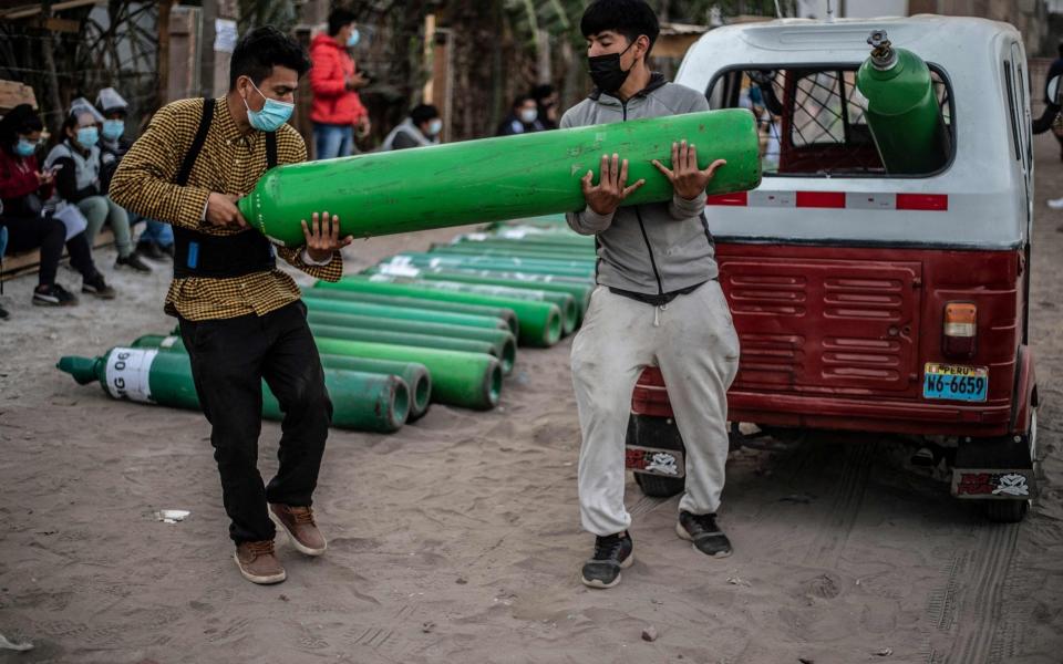 Men carry an empty oxygen tank as they arrive to queue to refill it in Villa El Salvador, on the southern outskirts of Lima - ERNESTO BENAVIDES / AFP