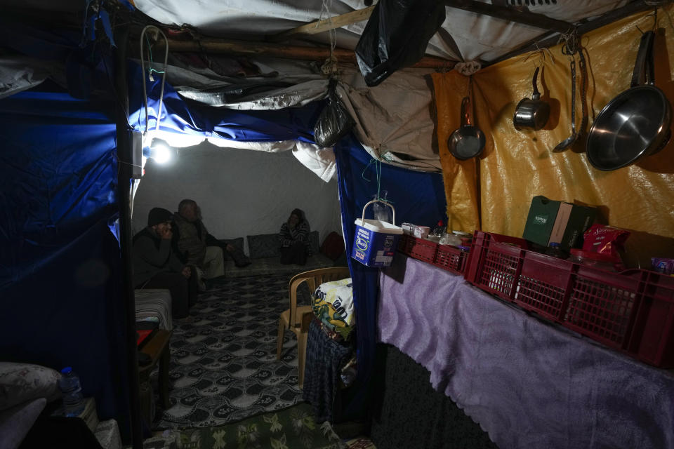 Earthquake survivor Rafet Donmez, center, sits on mattresses with his wife and son inside a tent in Antakya, southern Turkey, Friday, Jan. 12, 2024. A year after a powerful earthquake hit on Feb. 6, 2023, families who do not qualify for container homes are sheltering in tents, too afraid to return to homes that authorities have listed as being slightly damaged. (AP Photo/Khalil Hamra)