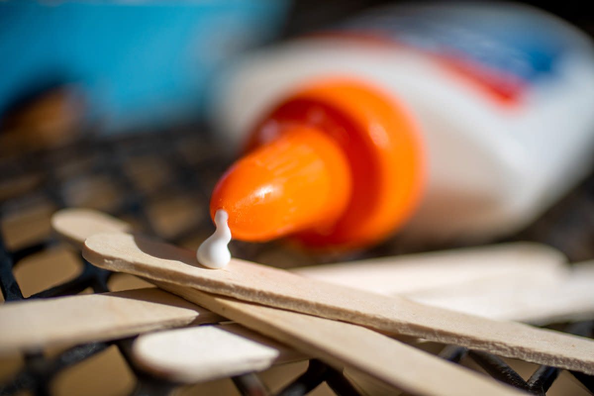 Elmers glue sits sideways with glue coming out and hidden wooden sticks. 