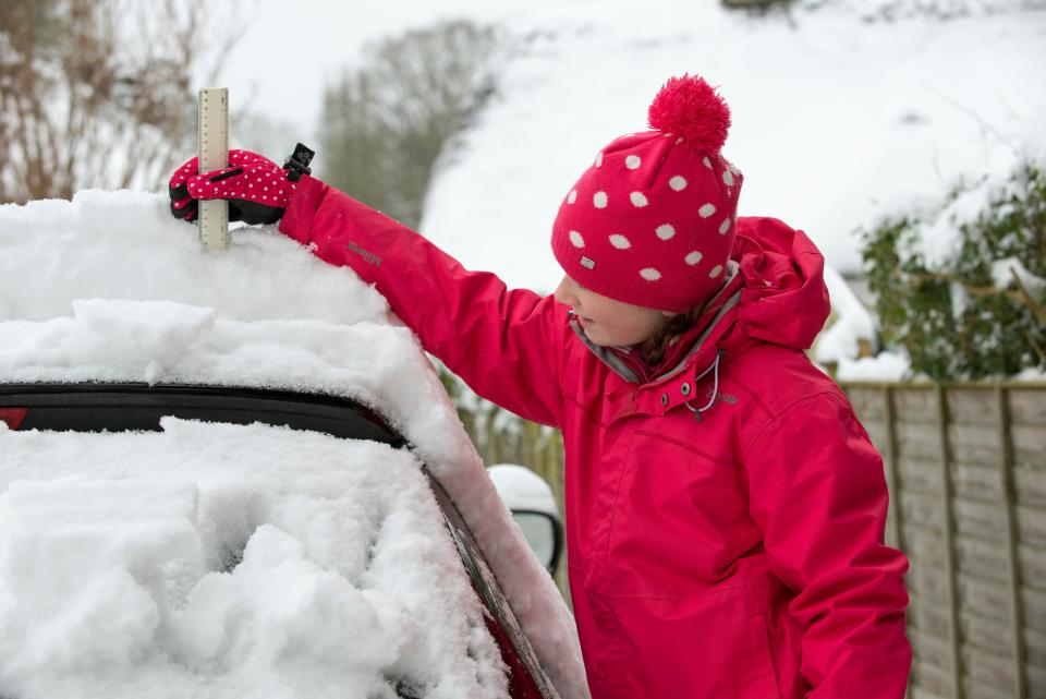 Young girl checks the snow depth on a car using a ruler