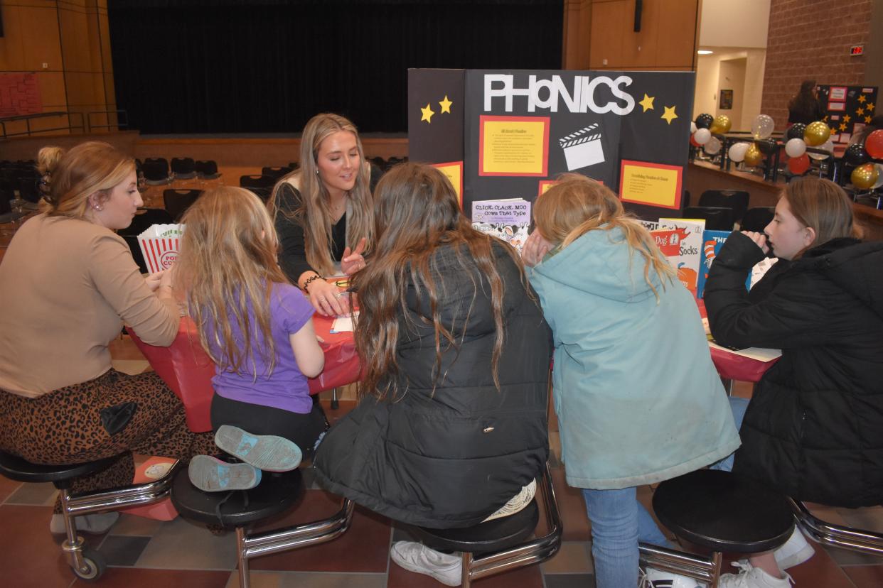 Adrian College elementary teacher education students Madelyn Peters, facing camera, and Summer Gaines, seated at left, talk about phonics to Addison Elementary School students during a literacy night program Tuesday at Addison Middle/High School.