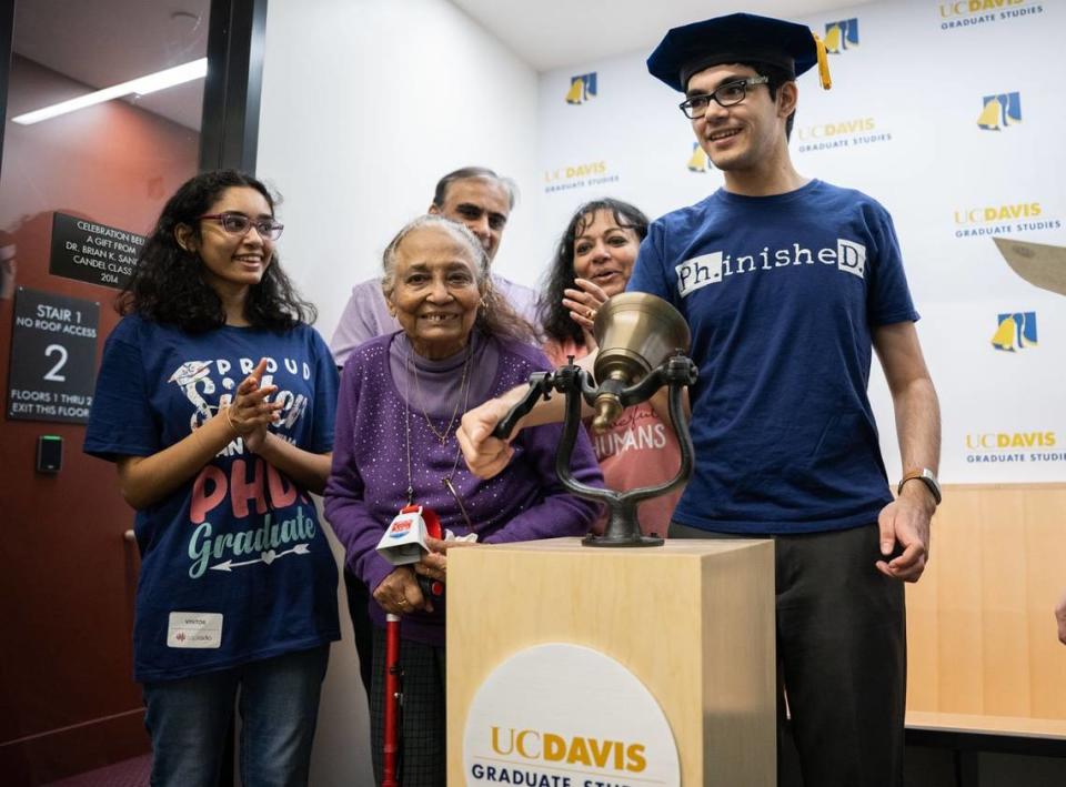 Tanishq Mathew Abraham, 19, celebrates the completion of his Ph.D. with family and friends by ringing the bell at the Graduate Center in Walker Hall, a UC Davis tradition for graduates who got their Ph.D. conferral letter, on Tuesday, June 6, 2023. He is joined by his sister Tiara Abraham, left, grandmother Thankam Mathew, who also holds a Ph.D. in veterinary medicine, father Bijou Abraham and mother Taji Abraham.