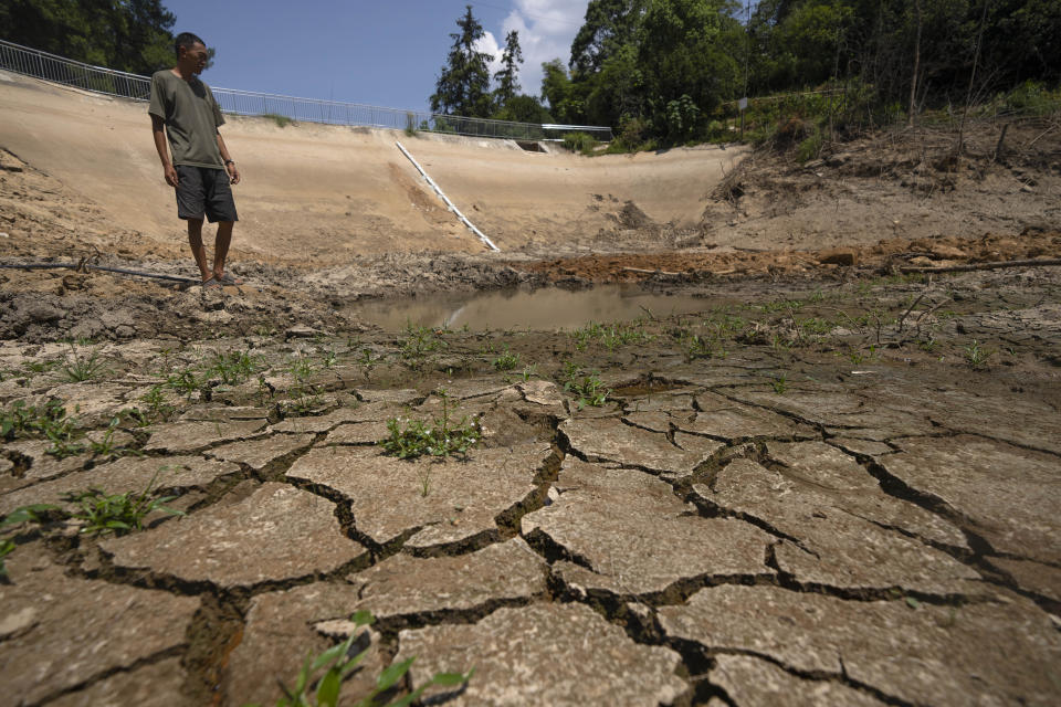 Gan Bingdong stands in the basin of a community reservoir near his farm that ran nearly empty after its retaining wall started to leak and hot weather and drought conditions accelerated the loss of water, in Longquan village in southwestern China's Chongqing Municipality, Saturday, Aug. 20, 2022. Drought conditions across a swathe of China from the densely populated east across central farming provinces into eastern Tibet have "significantly increased," the national weather agency said Saturday. The forecast called for no rain and high temperatures for at least three more days from Jiangsu and Anhui provinces northwest of Shanghai, through Chongqing and Sichuan in the southwest to the eastern part of Tibet. (AP Photo/Mark Schiefelbein)