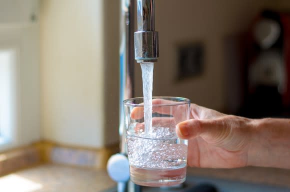 A hand filling up a glass of water under a faucet.