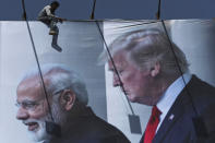 An Indian worker installs a giant hoarding welcoming U.S. President Donald Trump ahead of his visit, in Ahmadabad, India, Thursday, Feb. 20, 2020. Trump is scheduled to visit the city during his Feb. 24-25 India trip. (AP Photo/Ajit Solanki)